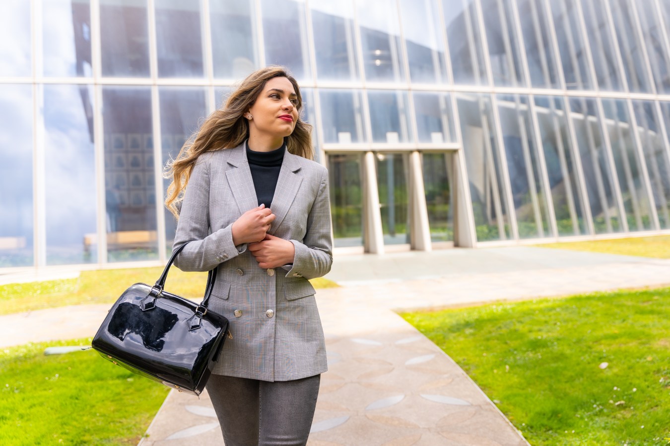 Portrait of a young businesswoman in a gray suit outside the office next to a glass building, leaving the office after finishing the working day