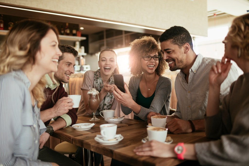 Picture of friends smiling and sitting in a cafe having coffee and using a phone