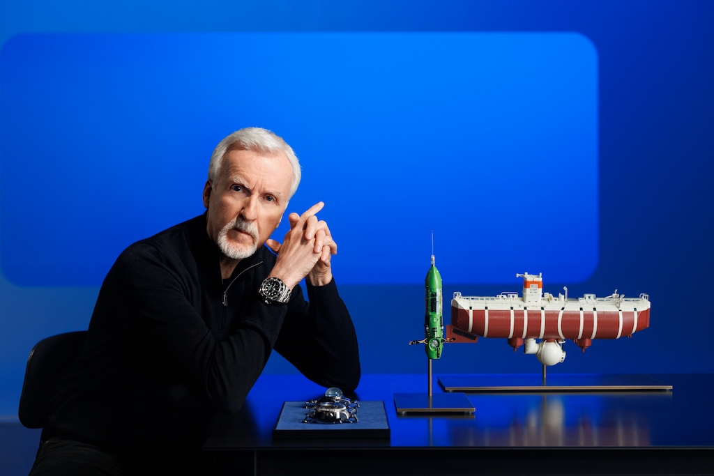 James Cameron, an Oyster Perpetual Deepsea Challenge on his wrist, posing with a model of the bathyscaphe Trieste (right), his submersible DEEPSEA CHALLENGER (centre) and (left) the two experimental watches attached to the vehicles during the dives into the Mariana Trench – respectively, the Deep Sea Special (behind) and the Rolex Deepsea Challenge (in front).